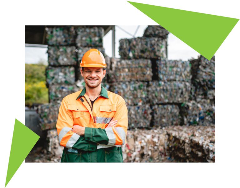 Smiling workman wearing PPE outdoors in front of compressed plastic waste for recycling at a plastic waste management facility.